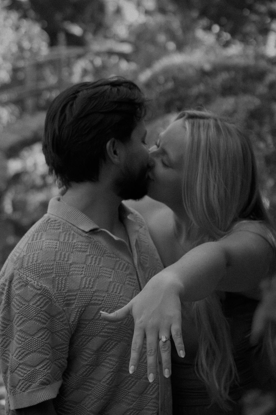 Black and white photo of Hailey showing her ring while kissing Alan